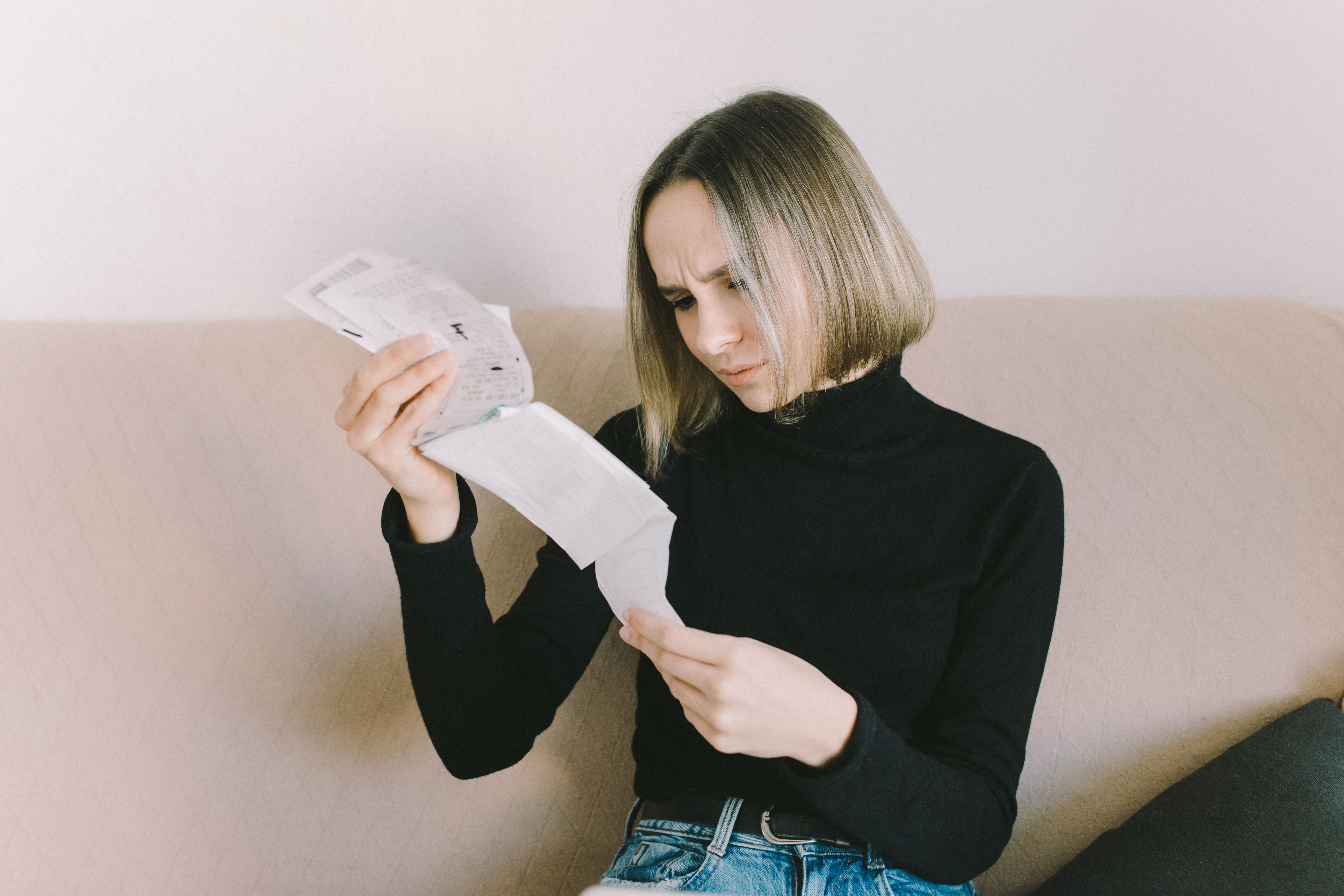 Concerned woman examining bills on a sofa indoors, representing rising living costs