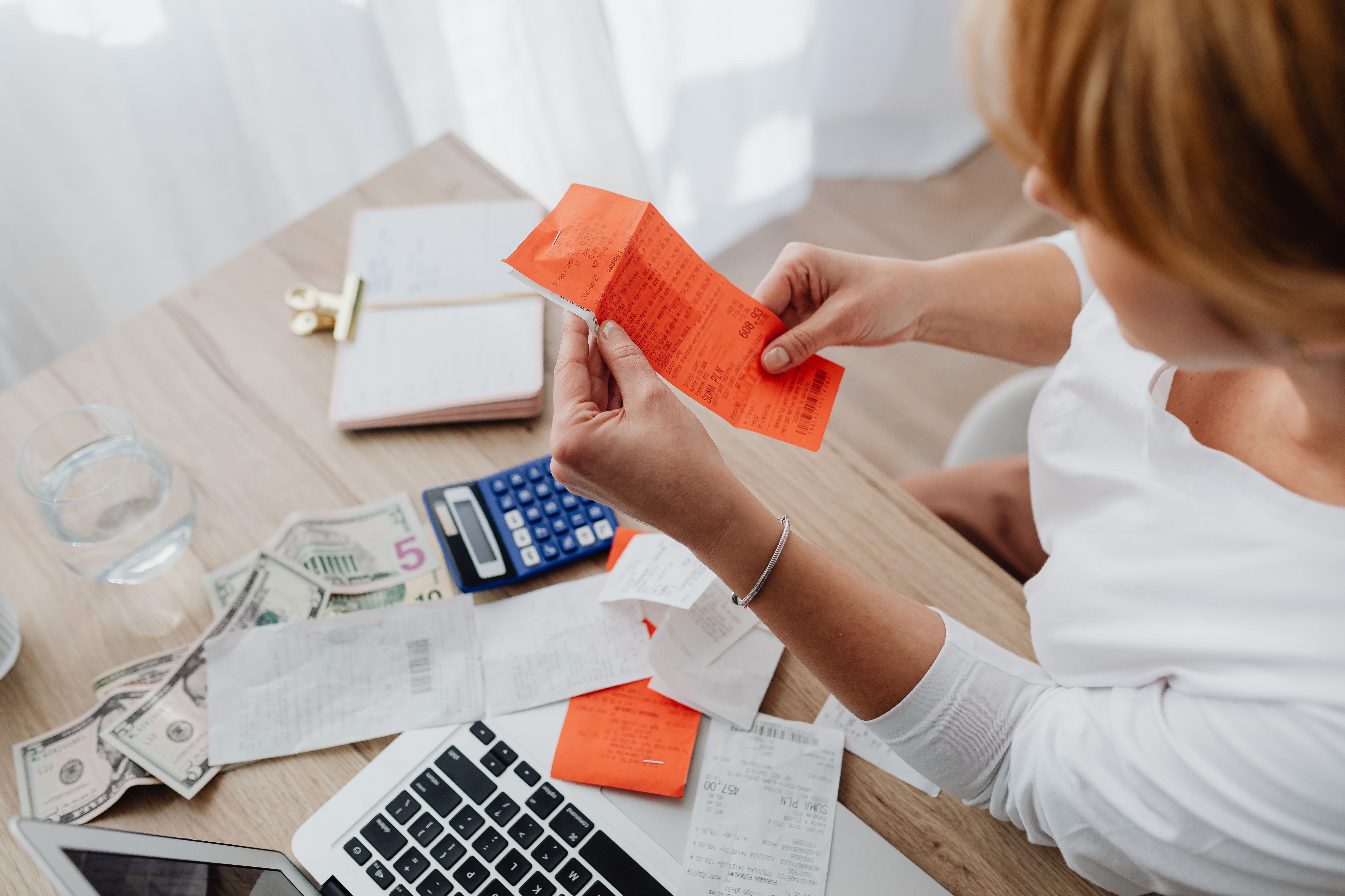 Woman using a calculator and receipts at a home office desk for household finance management