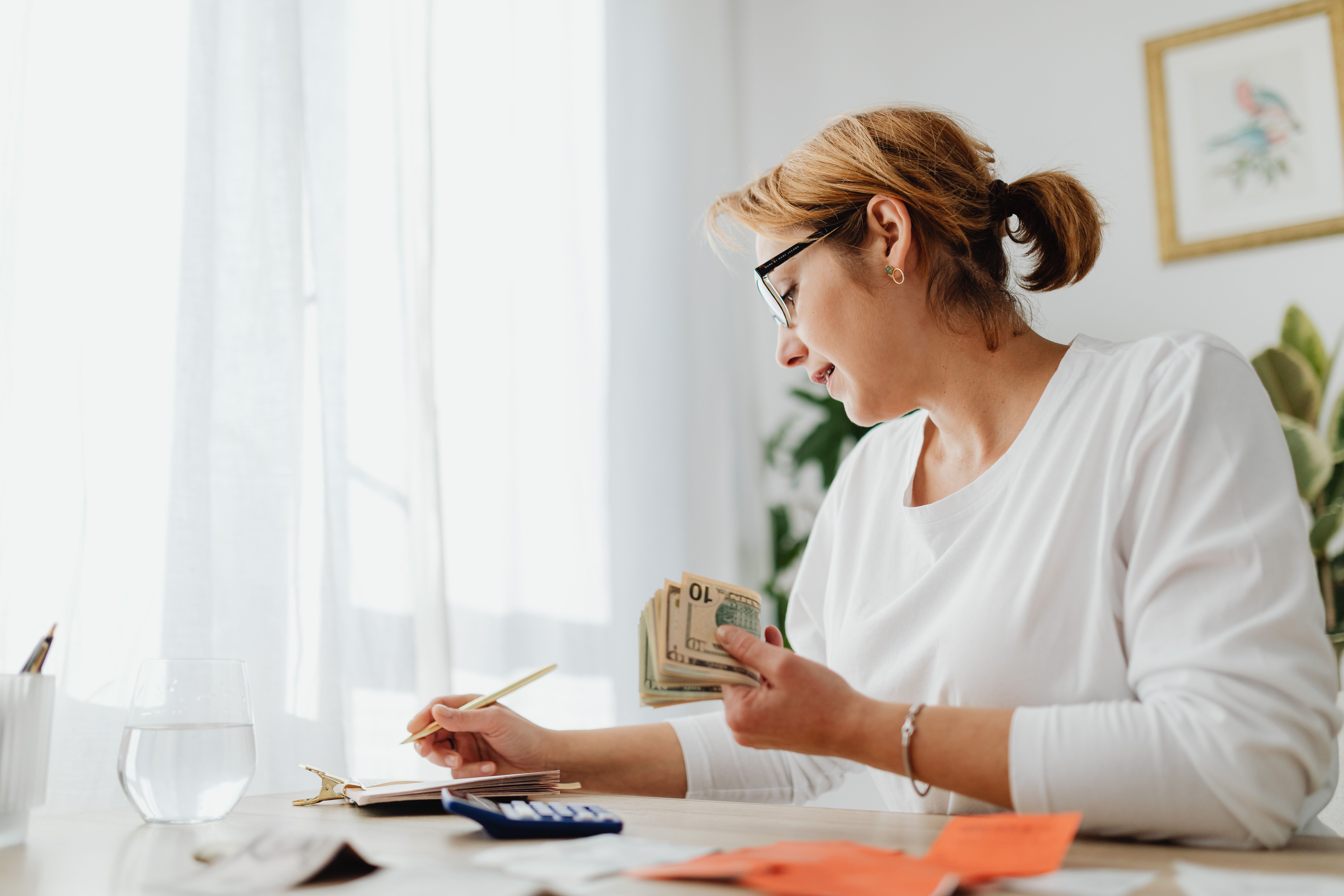 Businesswoman calculating finances with cash, calculator, and notebook at a bright desk